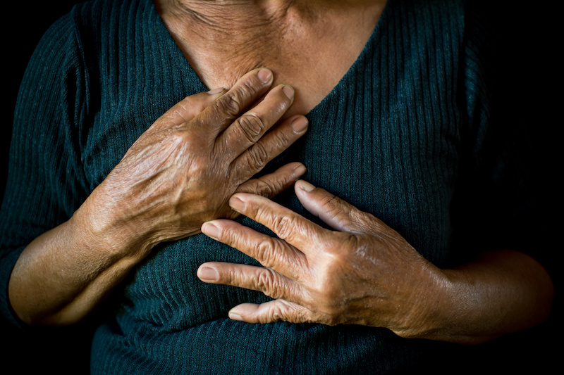 Old woman holding her hands to her chest on black background
