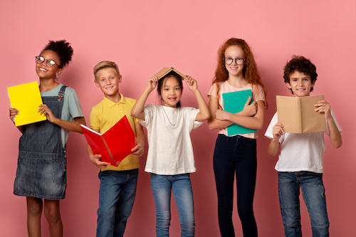 Portrait of smiling diverse kids with books and copybooks looking at camera, pink background